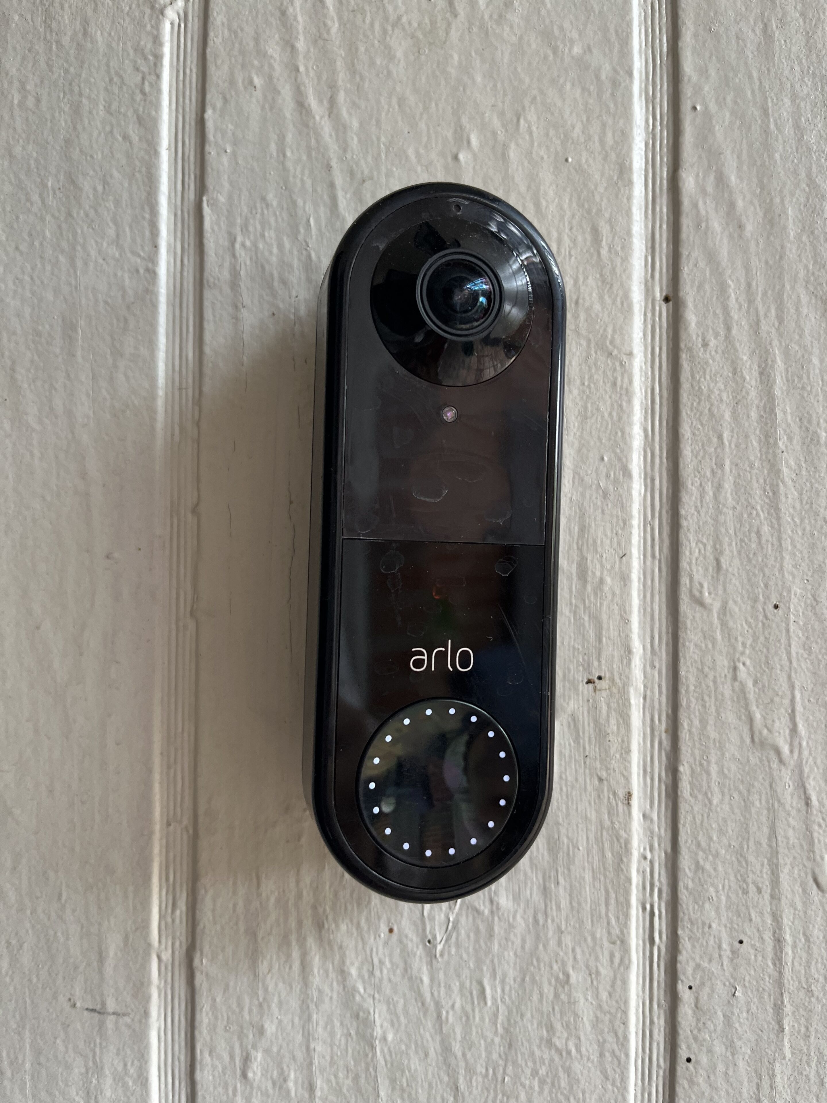 A black device with a camera and a circular button, labeled "arlo," mounted on a textured white door.