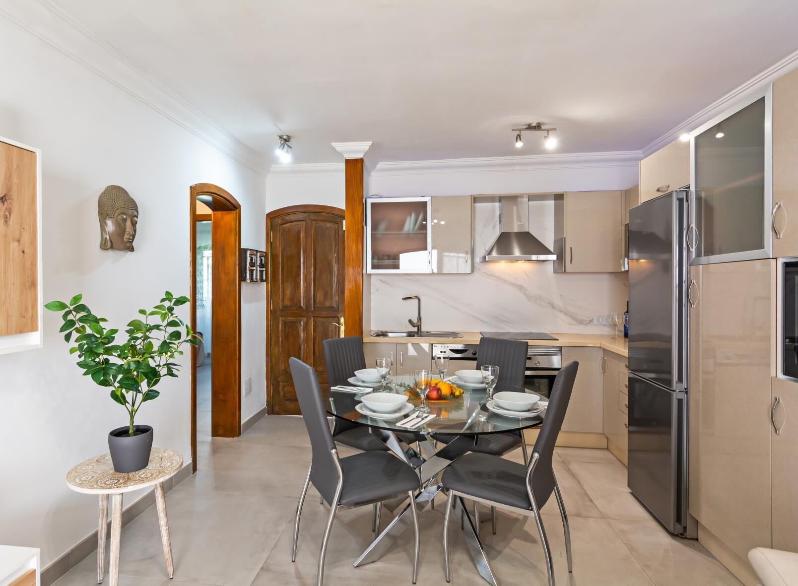 Une cuisine moderne avec un coin repas, comprenant un plan de travail en marbre, des appareils en acier inoxydable et une table à manger en verre avec des chaises.