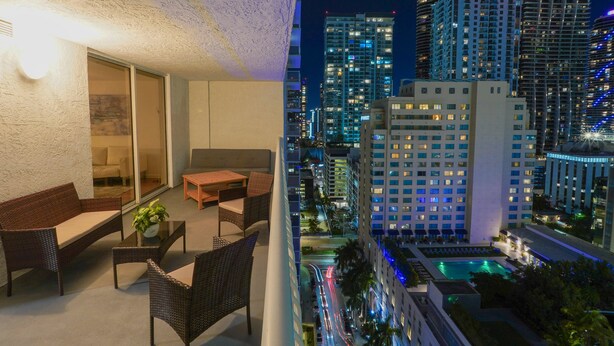 A balcony with wicker furniture and a view of a cityscape at night.