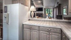 A kitchen with a white refrigerator, wooden cabinets, a tiled backsplash, and a window overlooking a garden. - Jen Casa Sue Casa - Spacious, Priv Hot Tub, TONS of Wildlife (Ruidoso)