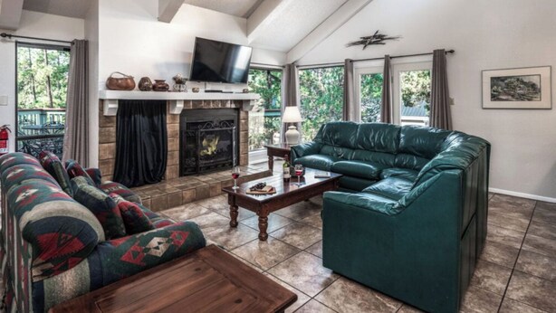 A spacious living room with a fireplace, a green leather sofa, a patterned couch, and a coffee table. - Jen Casa Sue Casa - Spacious, Priv Hot Tub, TONS of Wildlife (Ruidoso)