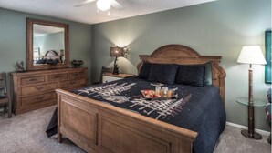 A bedroom with a wooden bed, a dresser, a nightstand, a ceiling fan, and a lamp. - Jen Casa Sue Casa - Spacious, Priv Hot Tub, TONS of Wildlife (Ruidoso)