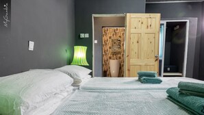 A bedroom with a bed, a green lamp, a wooden door, and a wall with a textured pattern. - Sea-front Suite - Sleeps 3 - Cape Point - Bakau (Bakau)