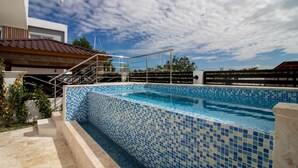 A swimming pool with blue mosaic tiles, a metal diving board, and a staircase leading to a covered area. - Homely 4BR Villa With Private Pool in Punta Cana (Punta Cana)