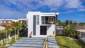 A modern two-story house with a balcony, a small garden, and a paved driveway. - Homely 4BR Villa With Private Pool in Punta Cana (Punta Cana)