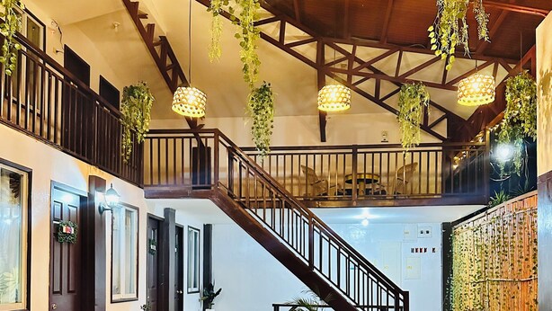 Un intérieur spacieux agrémenté d'un escalier en bois, de meubles en osier, de plantes suspendues et de luminaires suspendus.