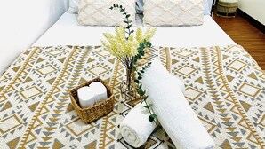 Un lit bien fait, avec une literie à motifs, un petit panier contenant une serviette enroulée et un vase rempli de fleurs.