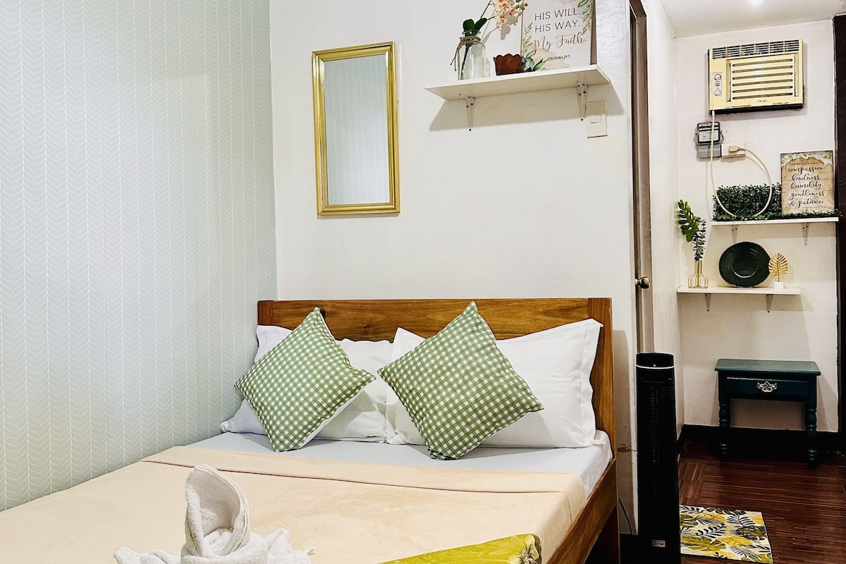 A neatly made bed with pillows, a bedside table, a mirror, and a shelf with decorative items.