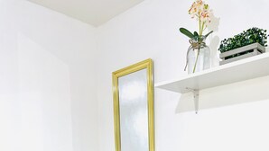 Une pièce avec un mur blanc, un miroir encadré, une chaise jaune et une étagère sur laquelle se trouvent une plante et un vase.