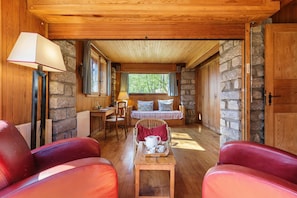 Una habitación acogedora con pared de piedra, techo de madera y cama con almohadas. Hay una mesa con una bandeja y una lámpara.