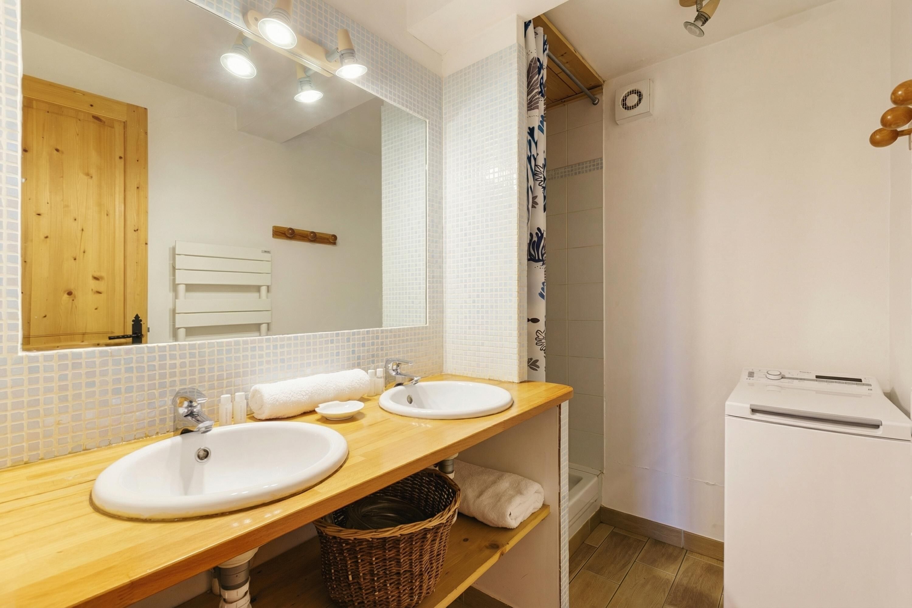 A bathroom with two sinks, a shower, a mirror, and a white washing machine.