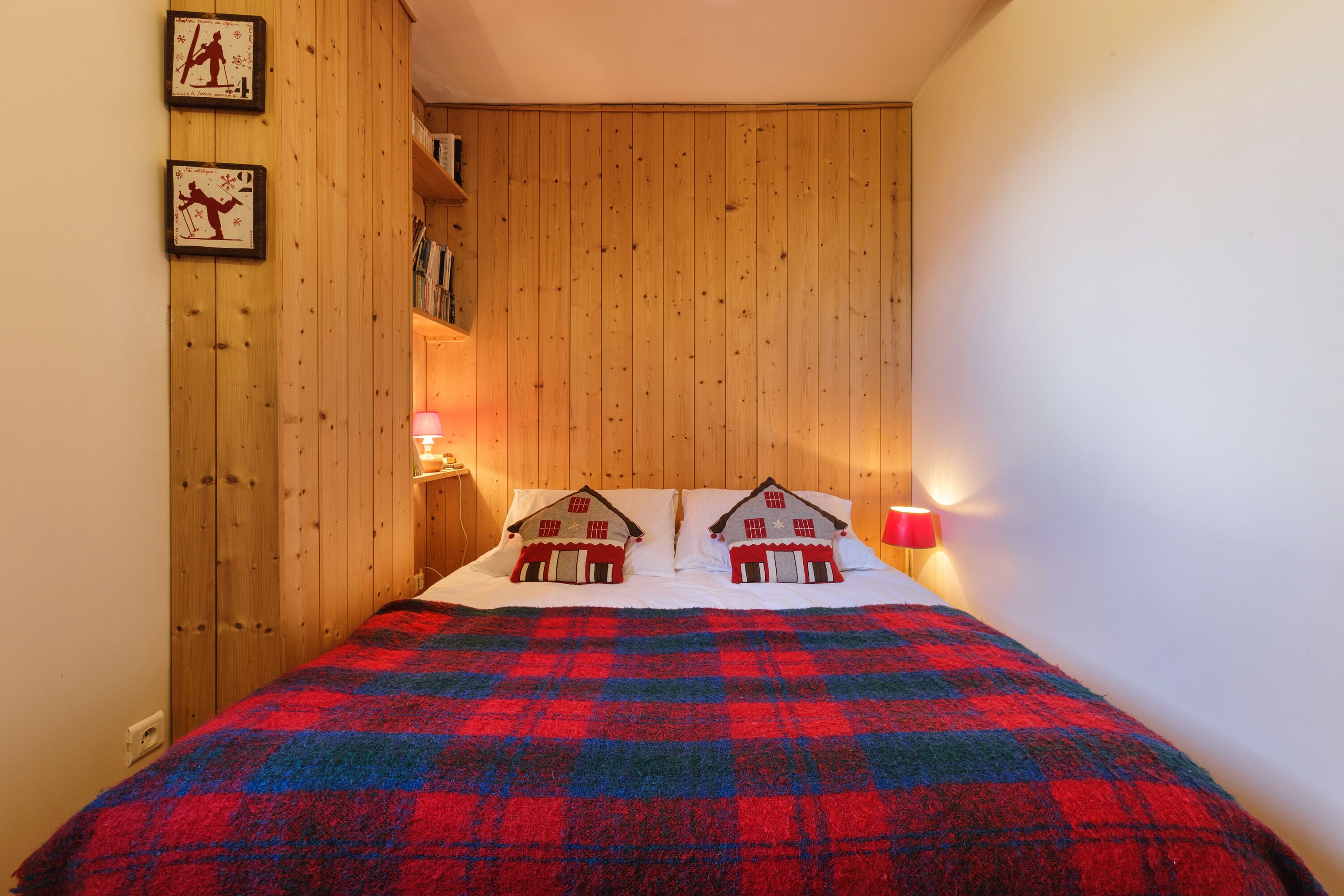 A bedroom with a wooden headboard, a plaid bedspread, and two wall-mounted lamps.