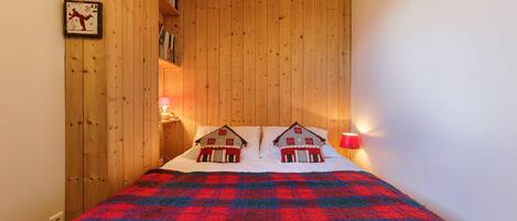 Une chambre à coucher avec une tête de lit en bois, une couvre-lit à carreaux et deux lampes fixées au mur.