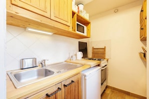 Una cocina con gabinetes de madera, un lavamanos de acero inoxidable, un microondas, una estufa y un refrigerador blanco.