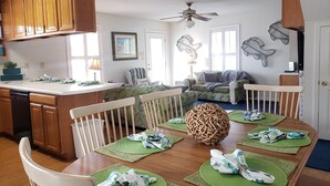 A dining area with a wooden table, green placemats, white chairs, and a decorative centerpiece. - Ocean Lakes Private Beach & Fountain View Tower (Myrtle Beach)
