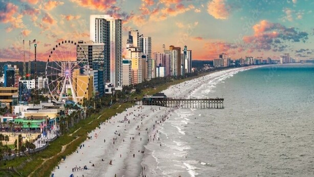 A beachside cityscape with a Ferris wheel, high-rise buildings, and a pier. - Ocean Lakes Private Beach & Fountain View Tower (Myrtle Beach)