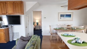 A cozy living room with a sofa, a dining table with chairs, and a kitchen area with cabinets and a TV. - Ocean Lakes Private Beach & Fountain View Tower (Myrtle Beach)