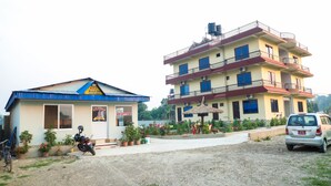 A hotel with a reception, a motorcycle parked in front, and a car parked nearby. - Hotel Nepal Inn (Sauraha)