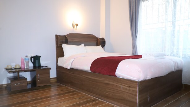 A neatly made bed with a wooden headboard, a bedside table with a water bottle, a kettle, and a cup. - Hotel Nepal Inn (Sauraha)