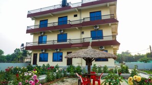 A multi-story building with balconies, air conditioning units, and a thatched umbrella in the courtyard. - Hotel Nepal Inn (Sauraha)