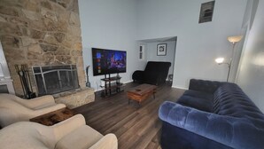 A living room with a stone wall, a fireplace, a TV, a black chair, a blue sofa, and a wooden coffee table.