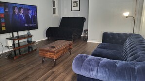 A living room with a TV, a black armchair, a blue sofa, and a wooden coffee table.