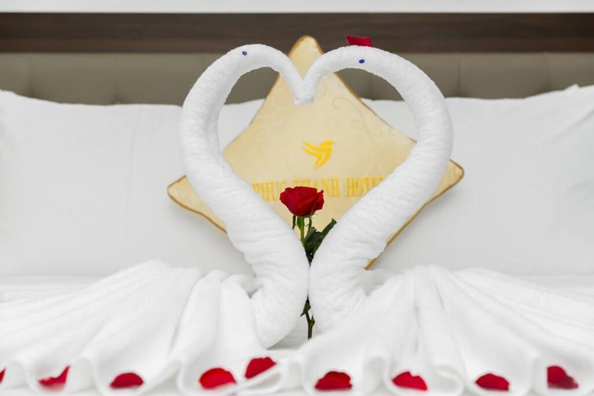 A bed with white linens and a heart-shaped towel arrangement.