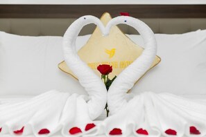 A bed with white linens and a heart-shaped towel arrangement.