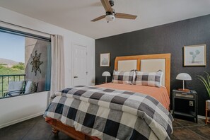 A bedroom with a bed, a ceiling fan, a nightstand, a lamp, and a window with a view.
