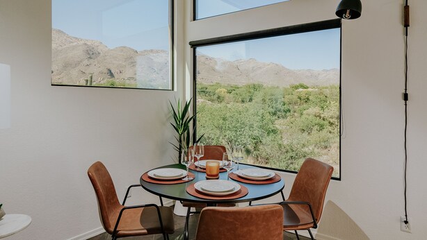A dining area with a table set for four, large windows offering a view of a desert landscape, and a modern pendant light.