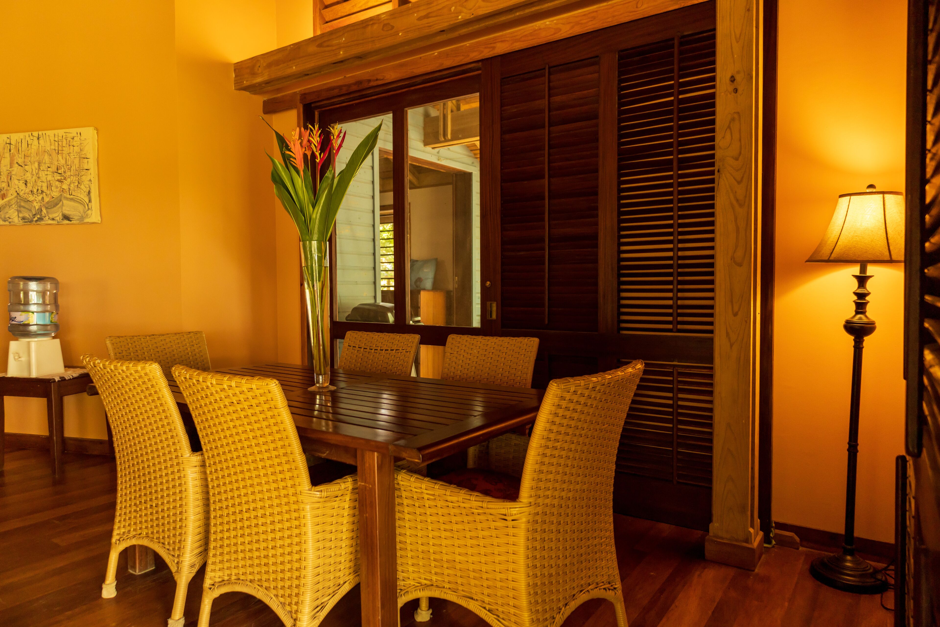 Un coin repas avec une table en bois et des chaises en osier, un vase rempli de fleurs et une lampe.