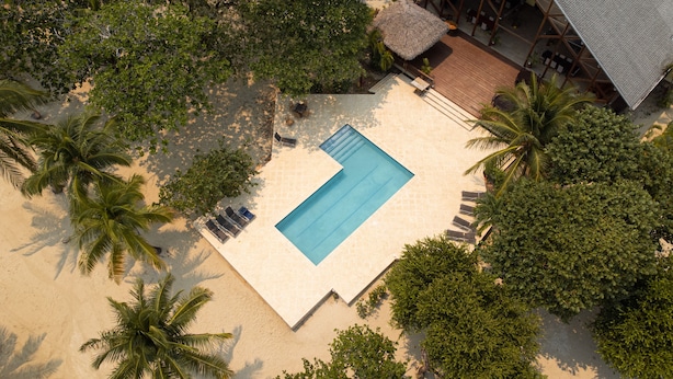 Vue aérienne d’un complexe hôtelier doté d’une piscine entourée de palmiers et d’une terrasse en bois.