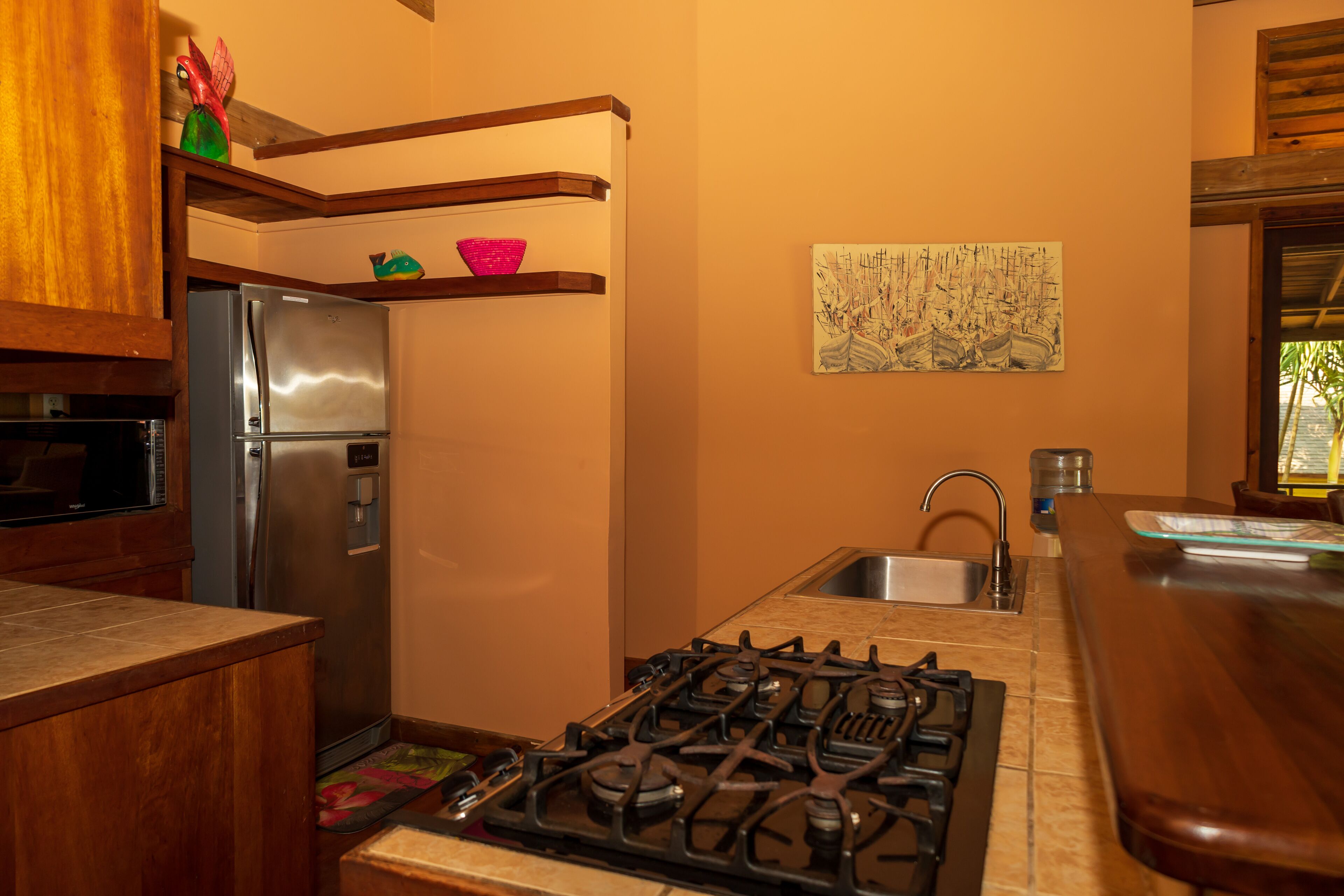 Una cocina con un refrigerador de acero inoxidable, una estufa a gas y repisas de madera sobre el lavamanos.