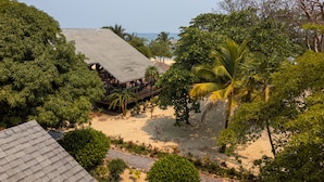Un complexe hôtelier situé en bord de mer, doté d’une structure en bois, de palmiers et offrant une vue dégagée sur l’océan.