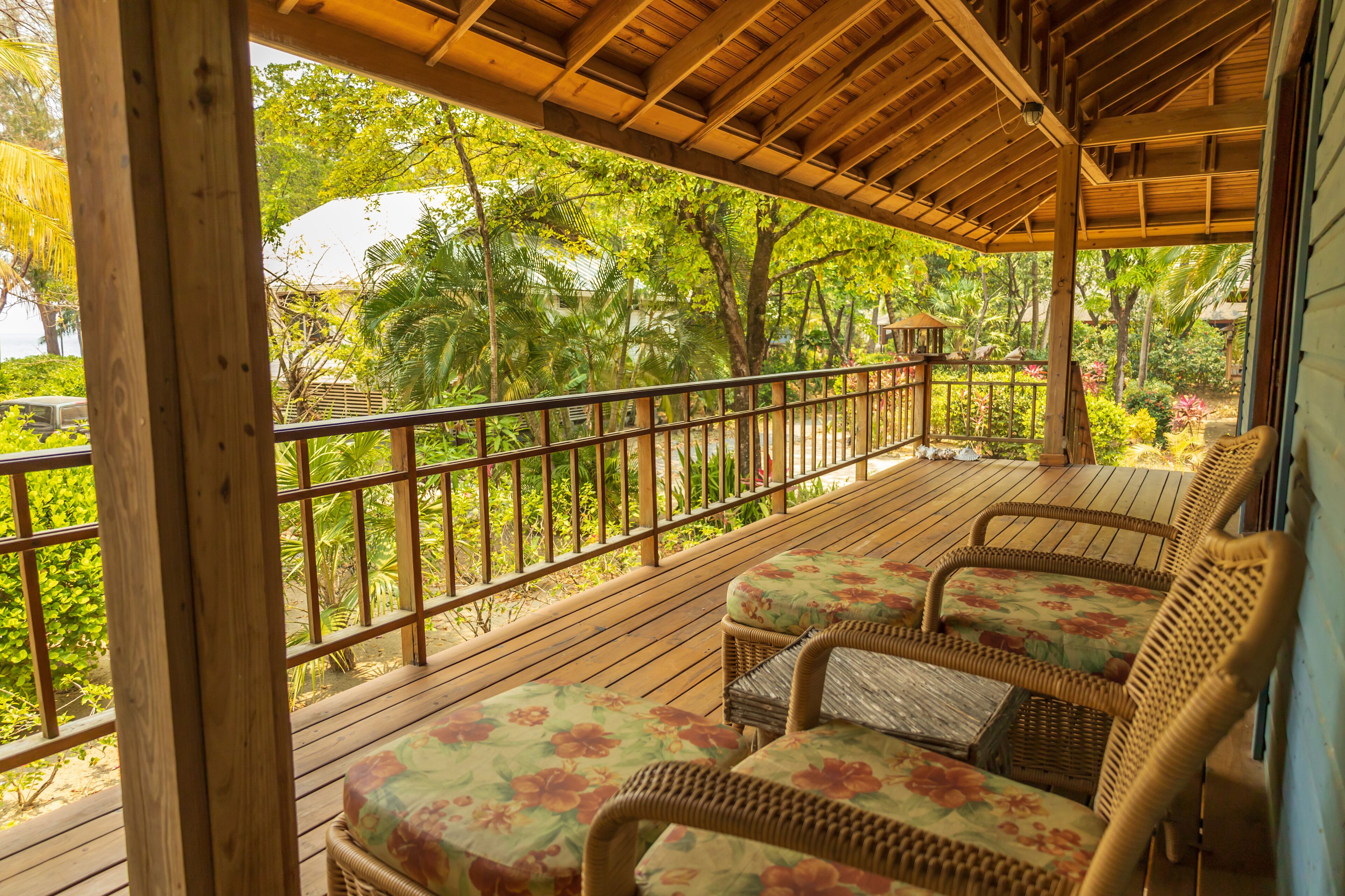 Terraza de madera con mobiliario de mimbre y vista a follaje tropical.