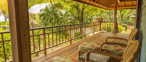 Terraza de madera con mobiliario de mimbre y vista a follaje tropical.