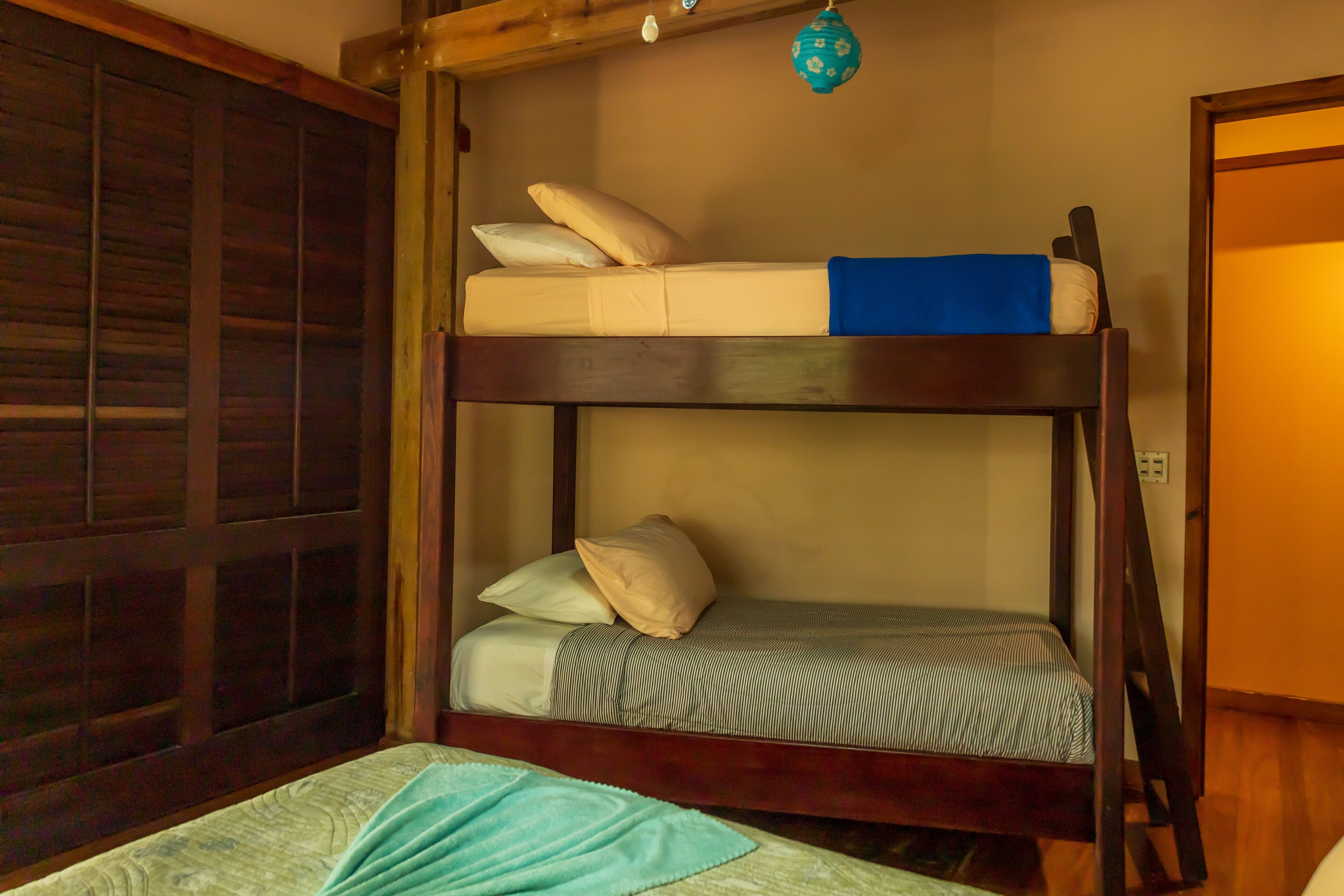 Una cama litera de dos niveles, un armario de madera y una lámpara colgante.