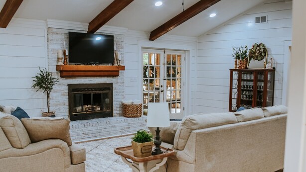 A cozy living room with a fireplace, a sofa, a TV mounted above the fireplace, and a bookshelf. - The Shanty @ Rayburn Country (Brookeland)