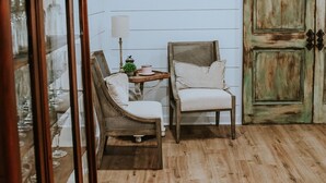 A room with wooden flooring, a white paneled wall, a rustic door, and two chairs with cushions. - The Shanty @ Rayburn Country (Brookeland)