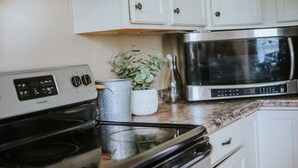 A kitchen with a stove, microwave, cabinets, and a potted plant. - The Shanty @ Rayburn Country (Brookeland)