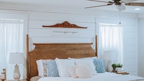 A bedroom with a wooden bed, a nightstand, a ceiling fan, and a wall-mounted sign. - The Shanty @ Rayburn Country (Brookeland)