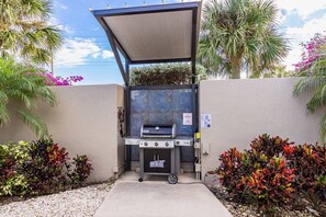 An outdoor grill area with a canopy, surrounded by plants and a wall. - Ocean Views! Across from Siesta Beach, Heated Pool (Siesta Key)