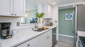 A modern kitchen with white cabinets, a coffee maker, a sink, and a refrigerator. - Ocean Views in Our House at the Beach, Full Gulf Views from Balcony, Heated Pools! (Siesta Key)