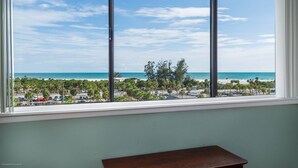A room with a large window overlooking a beach and parking area. - Ocean Views in Our House at the Beach, Full Gulf Views from Balcony, Heated Pools! (Siesta Key)