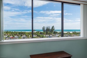 A room with a large window overlooking a beach and parking area. - Ocean Views in Our House at the Beach, Full Gulf Views from Balcony, Heated Pools! (Siesta Key)