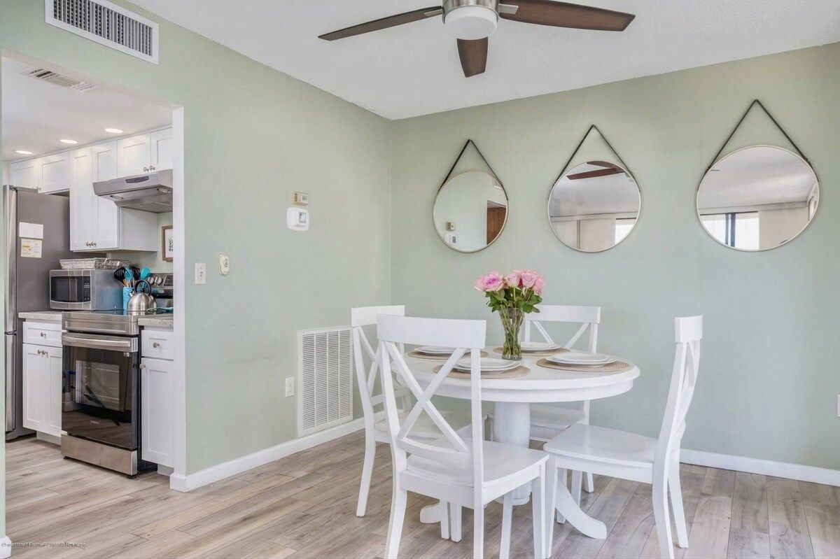 A dining area with a white table and chairs, a ceiling fan, and three wall-mounted mirrors.
