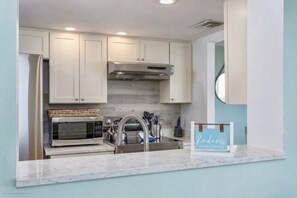 A modern kitchen with white cabinets, a stainless steel range hood, a microwave, and a sink.