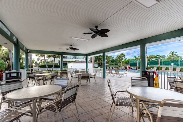 An outdoor patio area with tables and chairs, ceiling fans, and a view of a swimming pool.