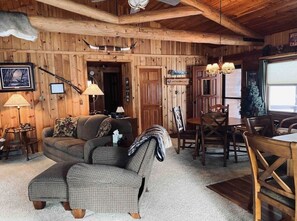 Un acogedor interior de cabaña con detalles de madera, un sofá, una mesa de comedor y una chimenea.