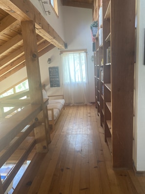 Un intérieur en bois avec un plafond haut, un canapé blanc, une bibliothèque et une fenêtre ornée de rideaux légers.